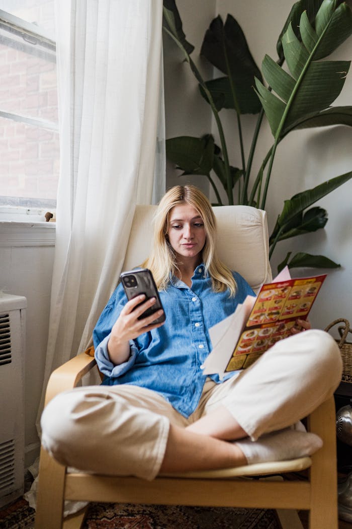 Woman sits comfortably in an armchair using a smartphone to order food.